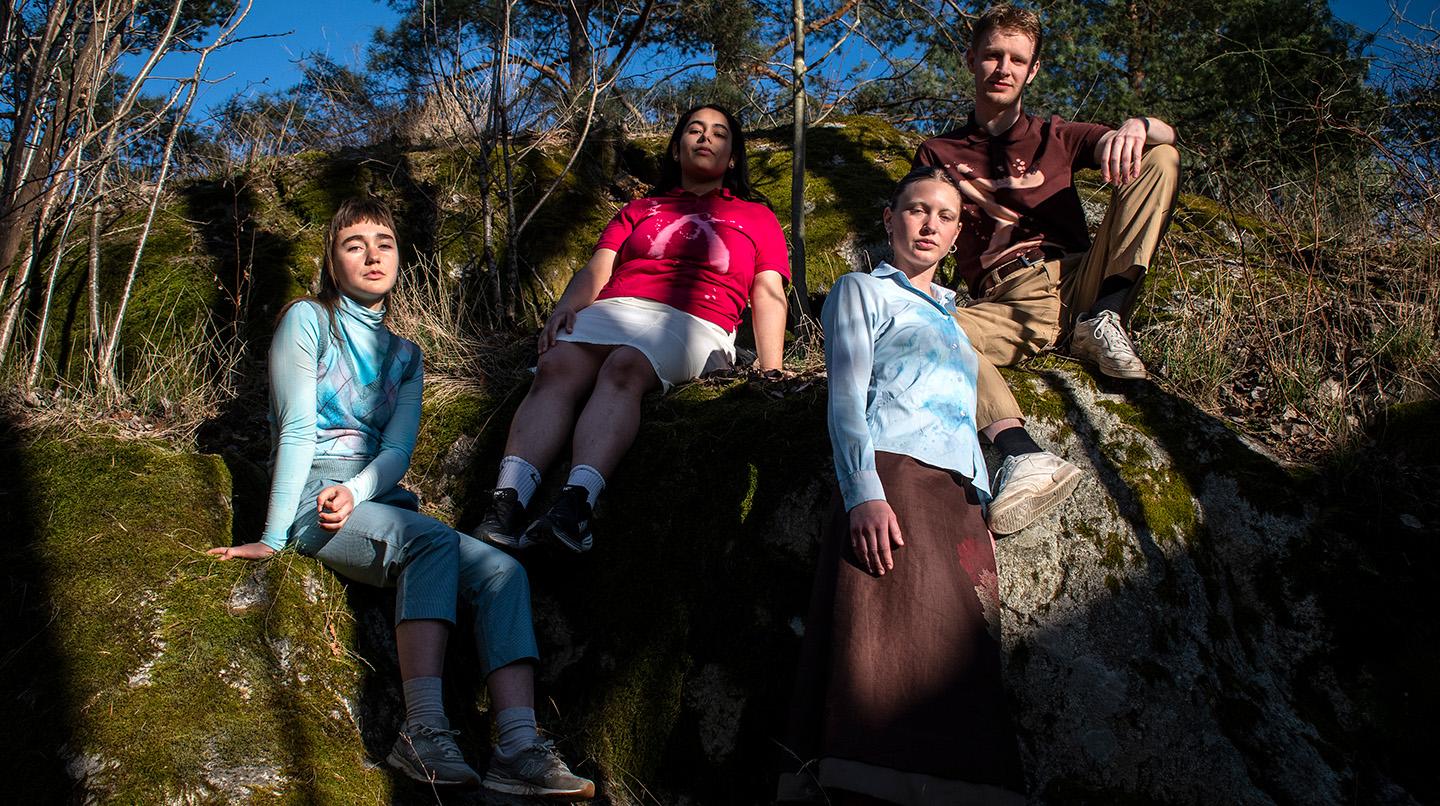 Fyra personer sitter på en sten i skogen.