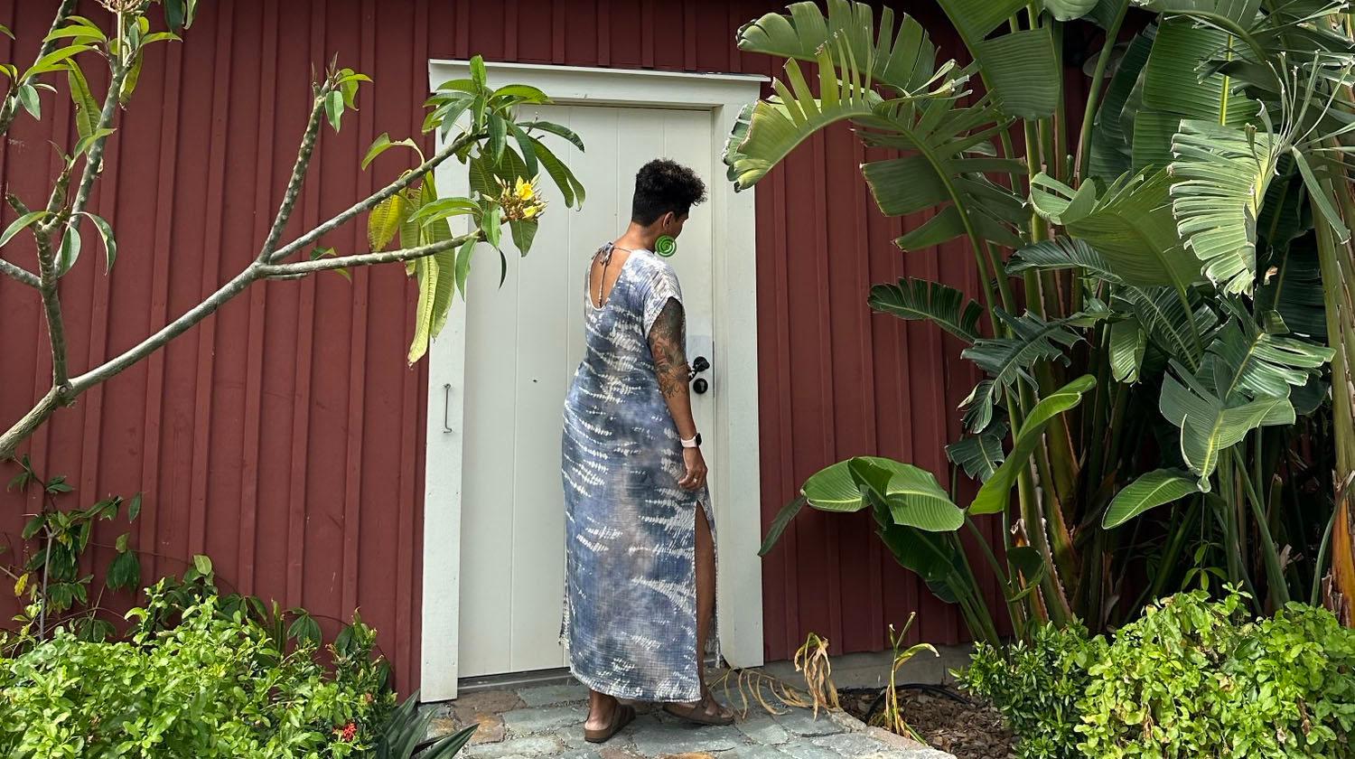 A person is standing outside a red house with a white door and seems to put his hand on the handle. 