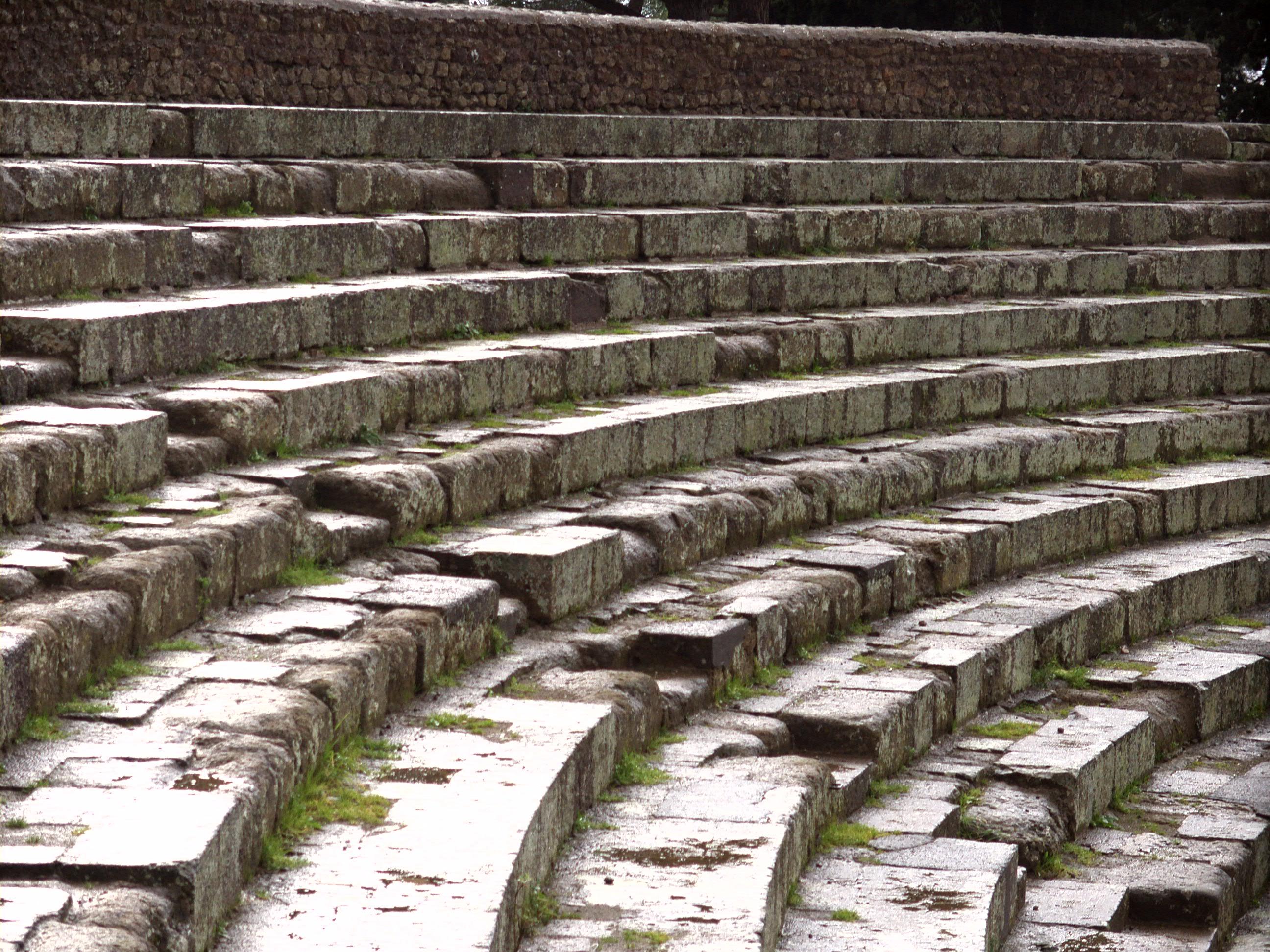 The audience section of an outdoor theater made of stone with grass growing out