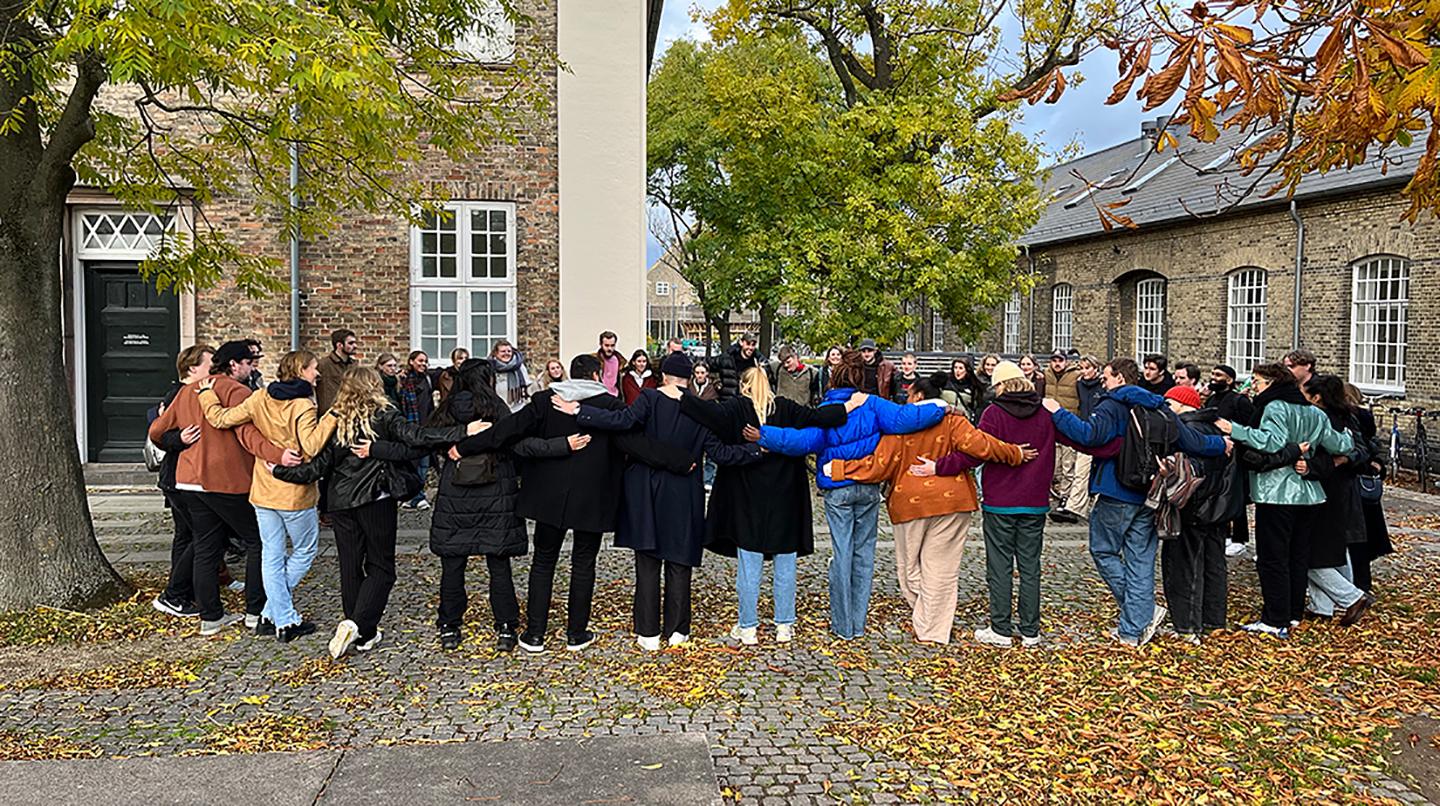 En grupp människor står i en ring utomhus och håller om varandras axlar